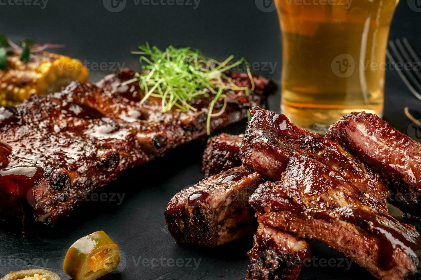 Pork ribs in barbecue sauce and a glass of beer on a black slate dish. A great snack to beer on a dark stone background. Top view with copy space photo