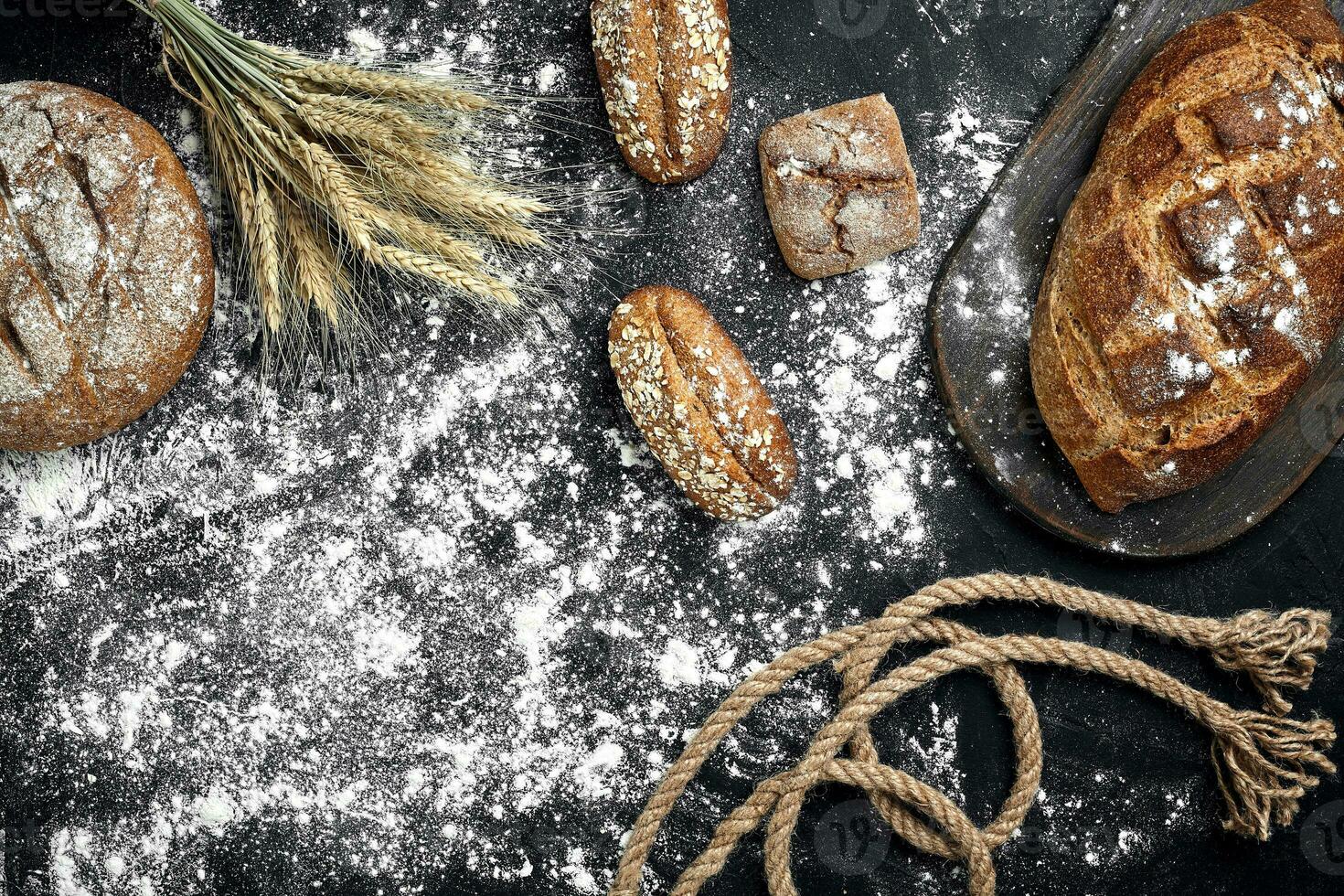 Different bread with flour and spikelets of wheaton black background photo