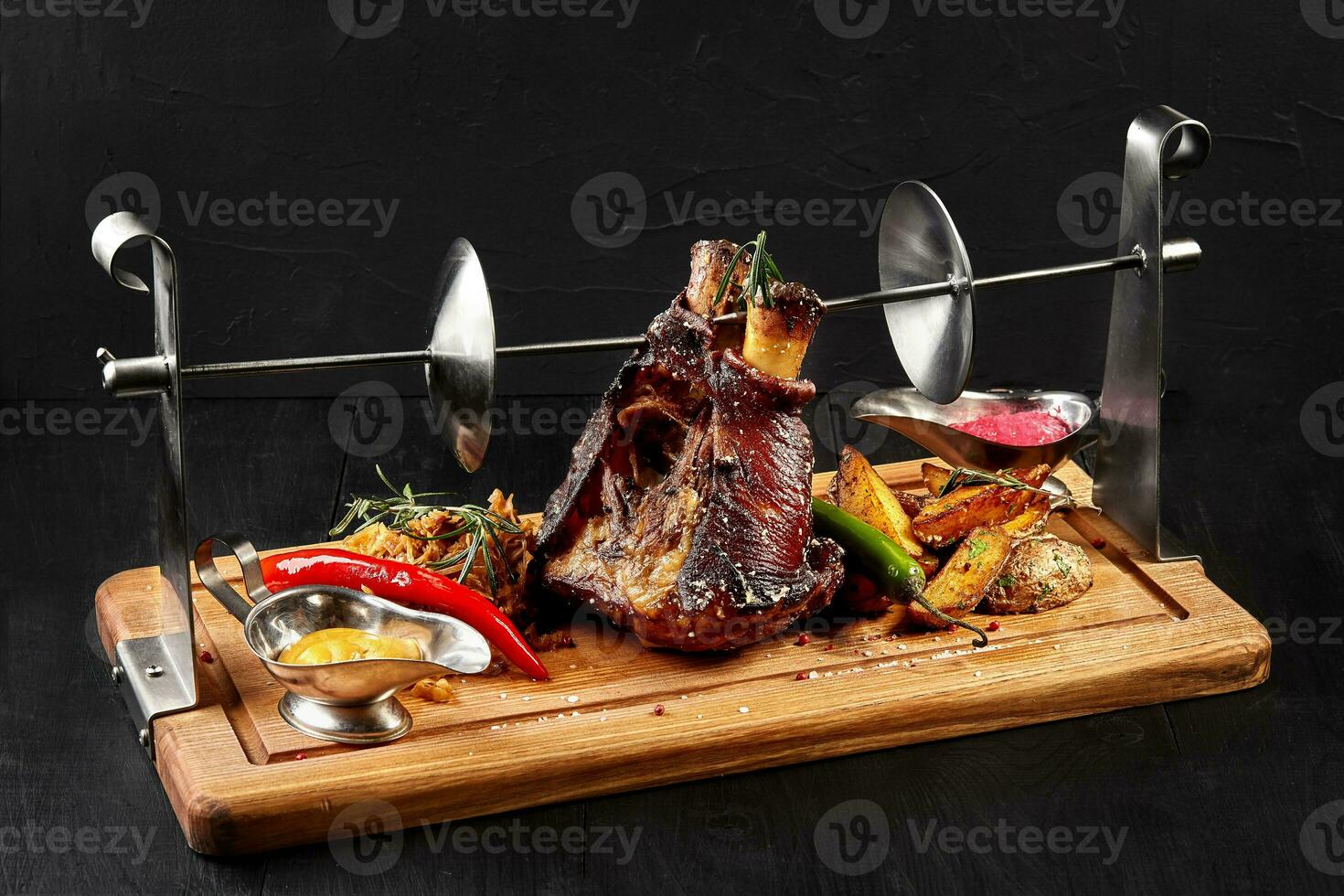 Roasted pork knuckle eisbein with braised boiled cabbage, potatoes, chili peppers and mustard on wooden cutting board, on a black background photo