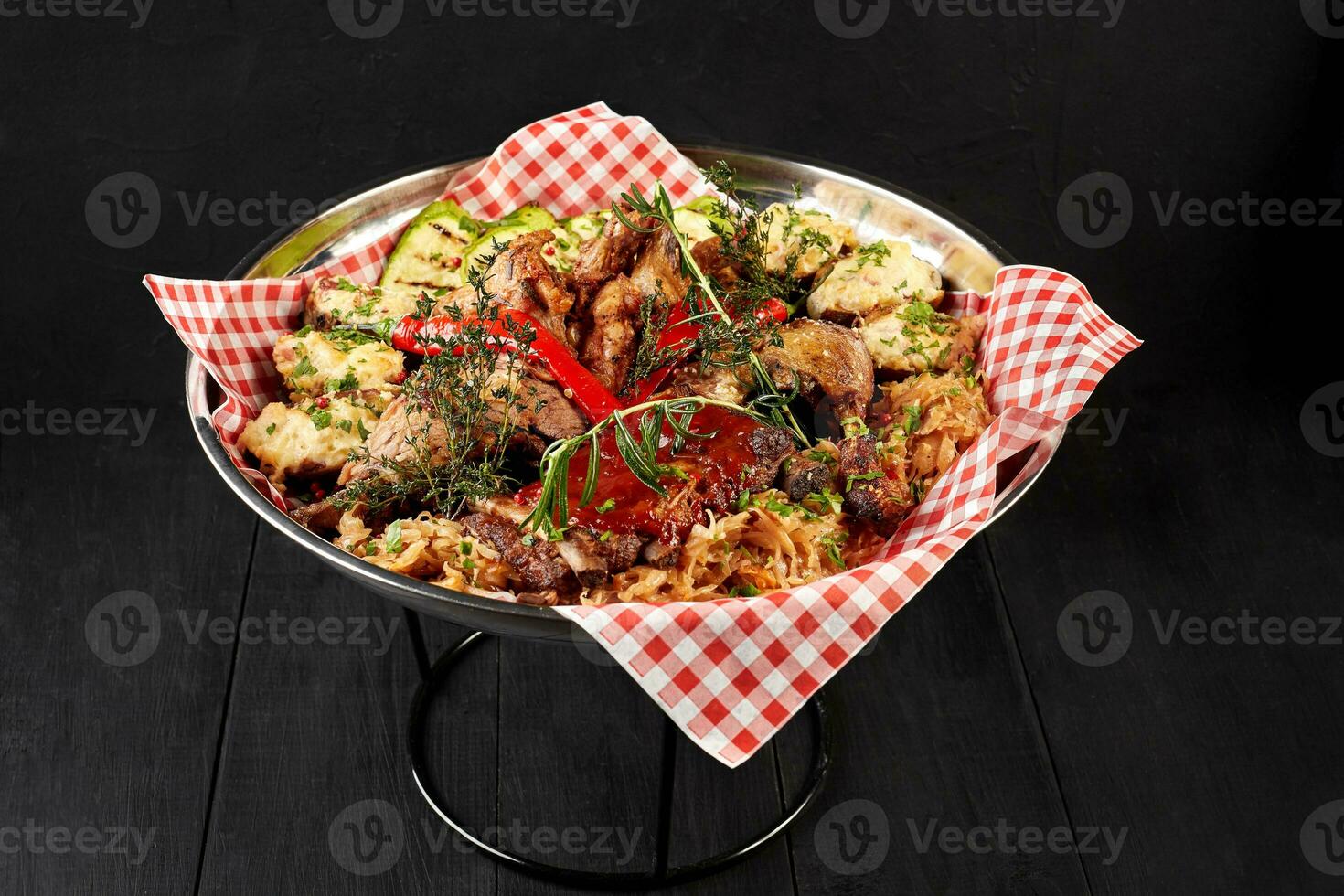 Assorted delicious grilled meat with vegetables and bbq sauce on an iron tray on black background close up. Big set of Hot Meat Dishes. Top view photo