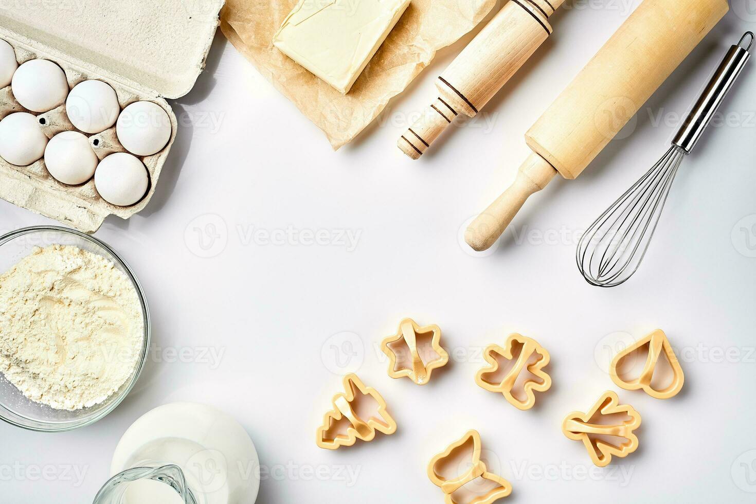 Objects and ingredients for baking, plastic molds for cookies on a white background. Flour, eggs, rolling pin, whisk, milk, butter, cream. Top view, space for text photo