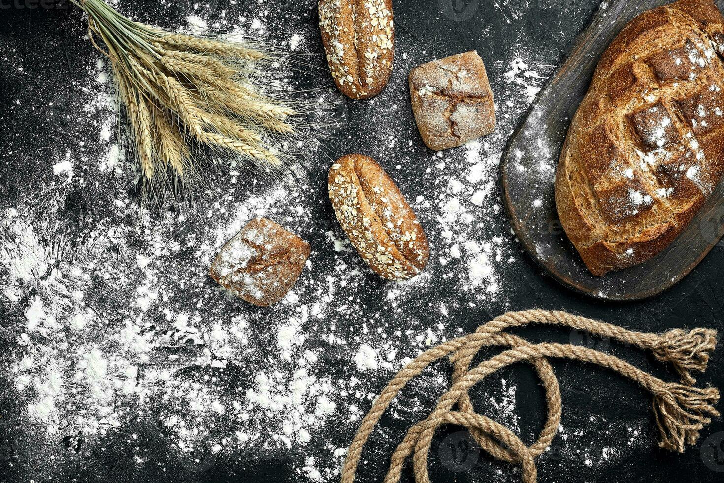 Different bread with flour and spikelets of wheaton black background photo