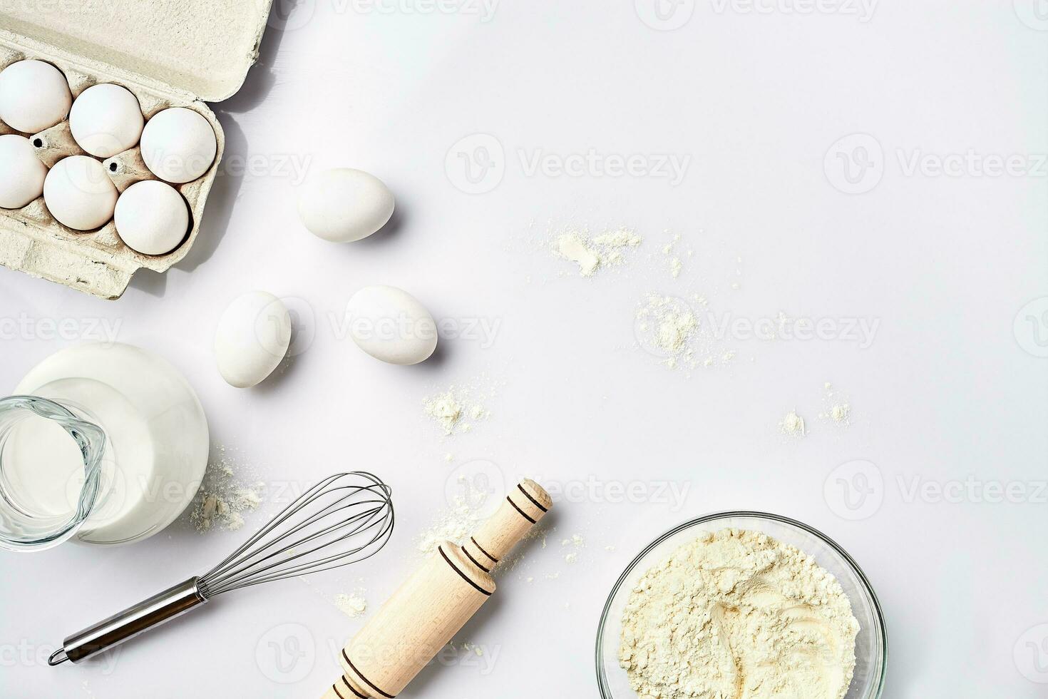 Wheat flour in the glass bowl, cream in a glass jar, chicken eggs - ingredients for the dough, top view photo