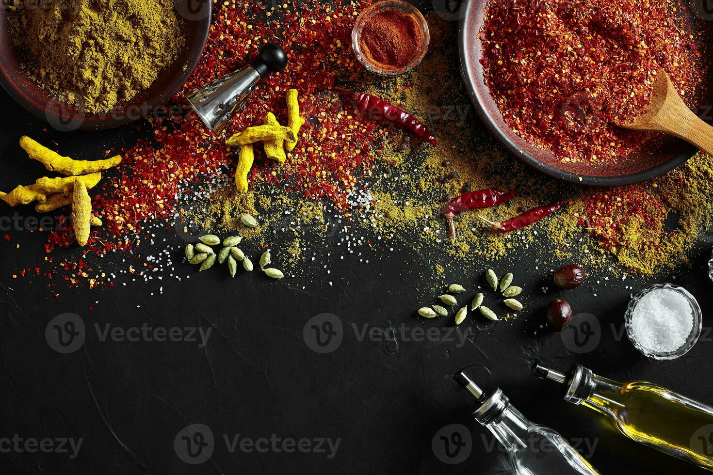 Cooking using fresh ground spices with big and small bowls of spice on a black table with powder spillage on its surface, overhead view with copyspace photo