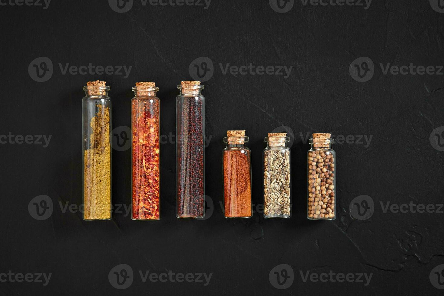 Cooking using fresh ground spices with six small jars of spice on a black table overhead view with copyspace photo