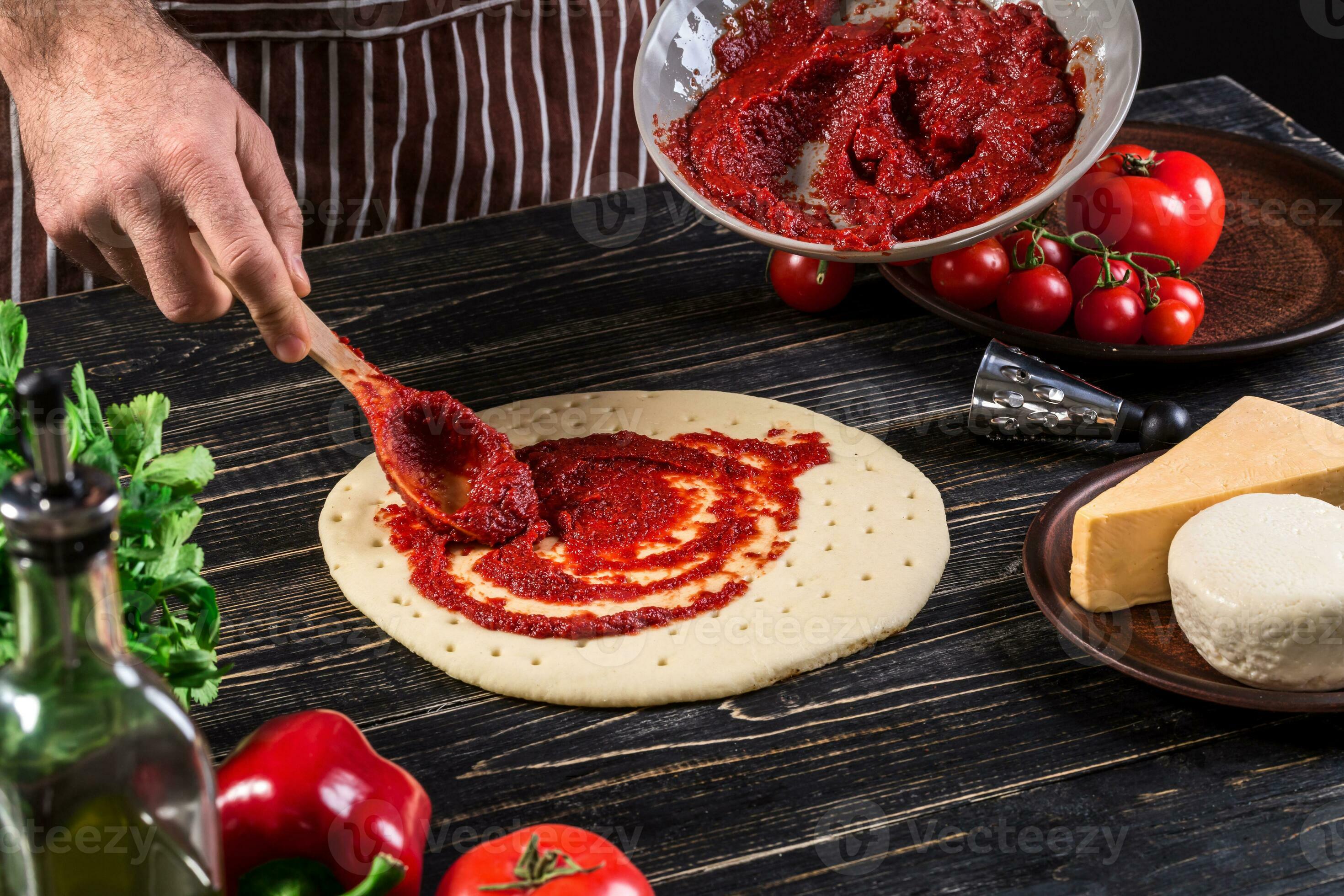 A male hand spreading tomato puree on a pizza base with spoon on an old