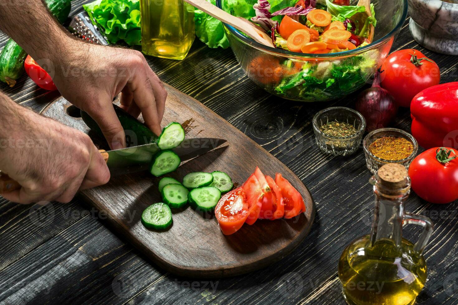 The man is cutting the cucumber in the kitchen in his house to prepare salad along with eating dinner. photo