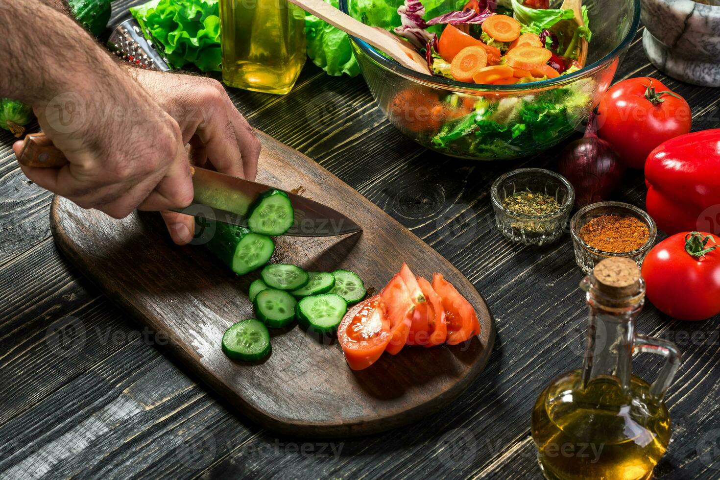 The man is cutting the cucumber in the kitchen in his house to prepare salad along with eating dinner. photo