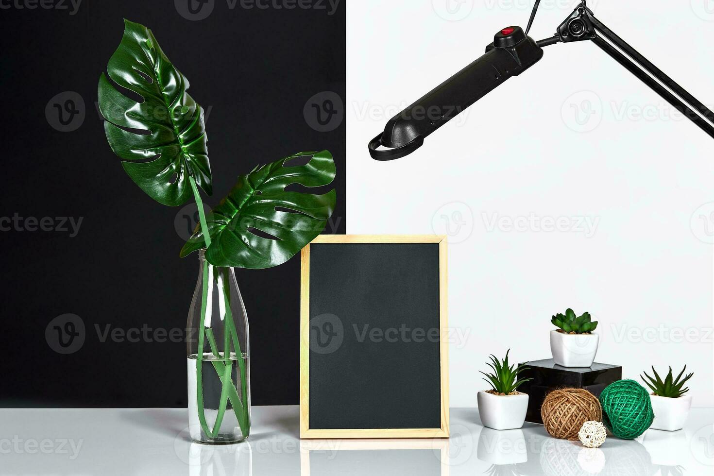 The stylish interior with mock up poster frame, leaves in glass bottle on table with black and white wall on background. photo