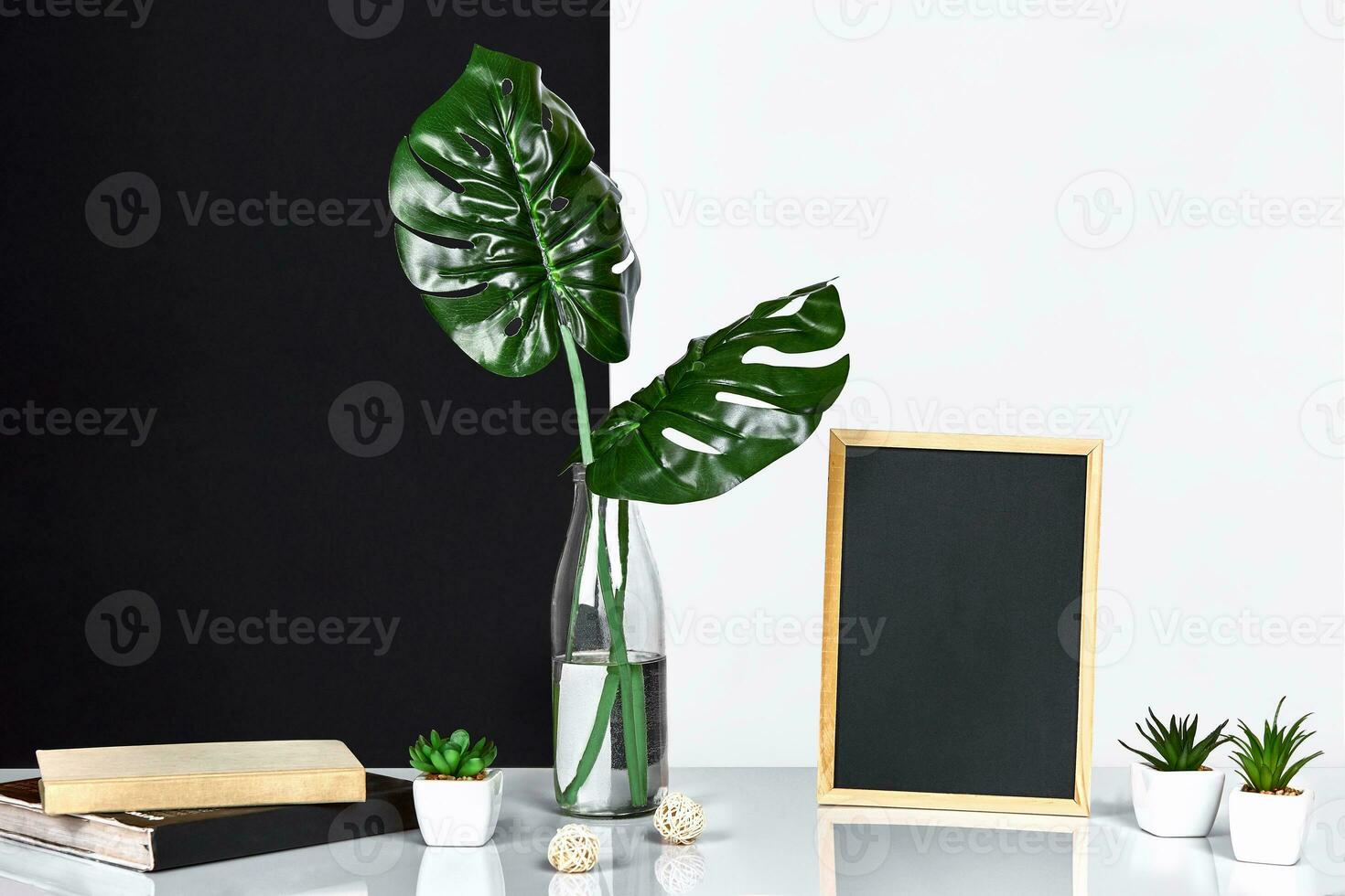 The stylish interior with mock up poster frame, leaves in glass bottle on table with black and white wall on background. photo
