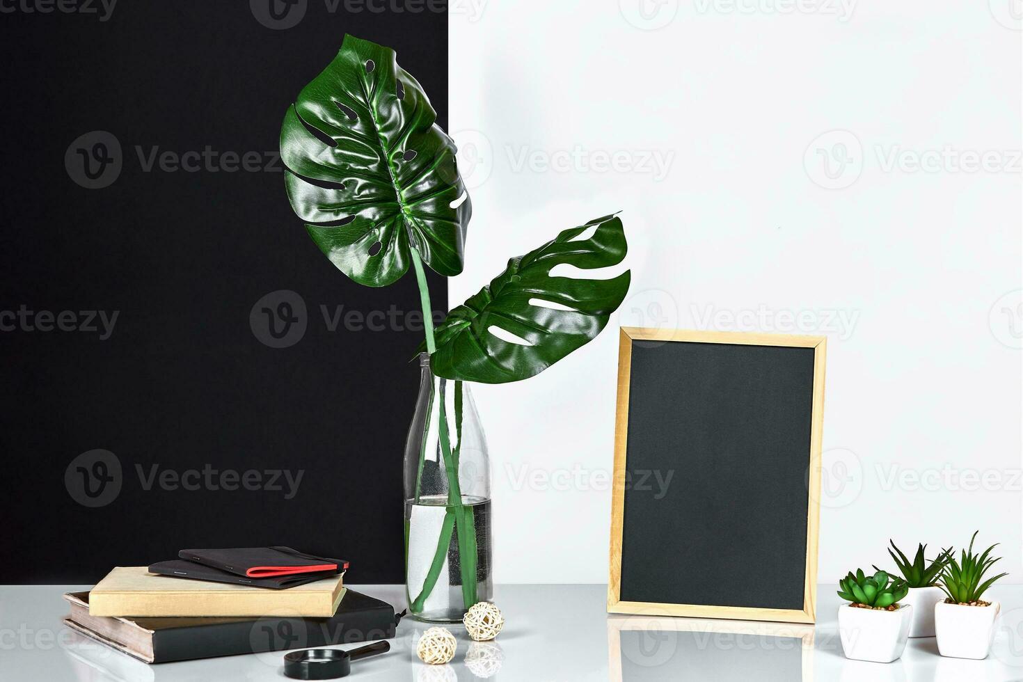 The stylish interior with mock up poster frame, leaves in glass bottle on table with black and white wall on background. photo