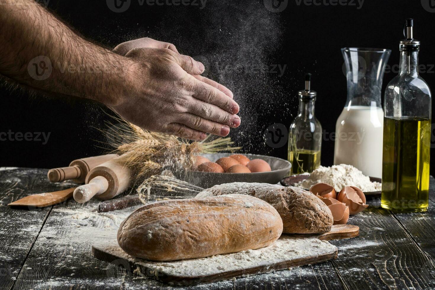 Chef sprinkles fresh bread with flour. Man preparing dough at table in kitchen. photo