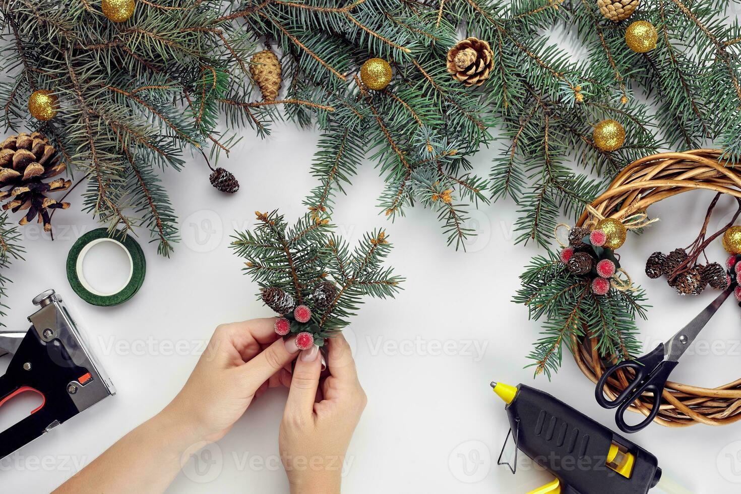 Top view of female hands make a Christmas wreath. Packed gifts and scrolls, spruce branches and tools on white table. photo