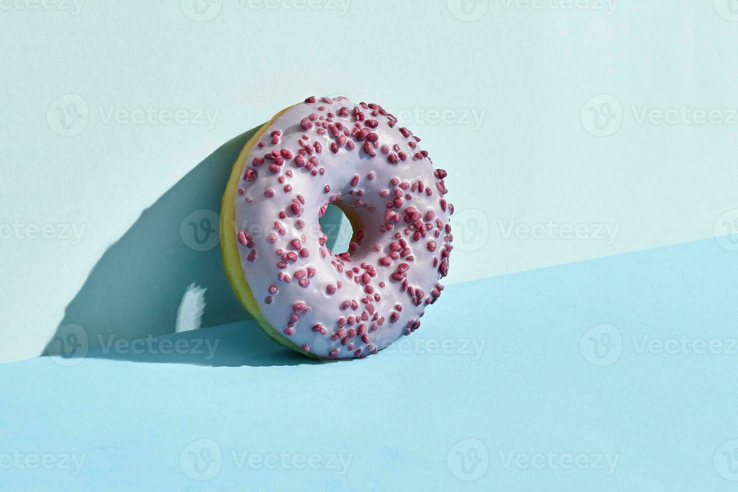 Food design. Close up high quality image of pink glazed donut on blue background photo