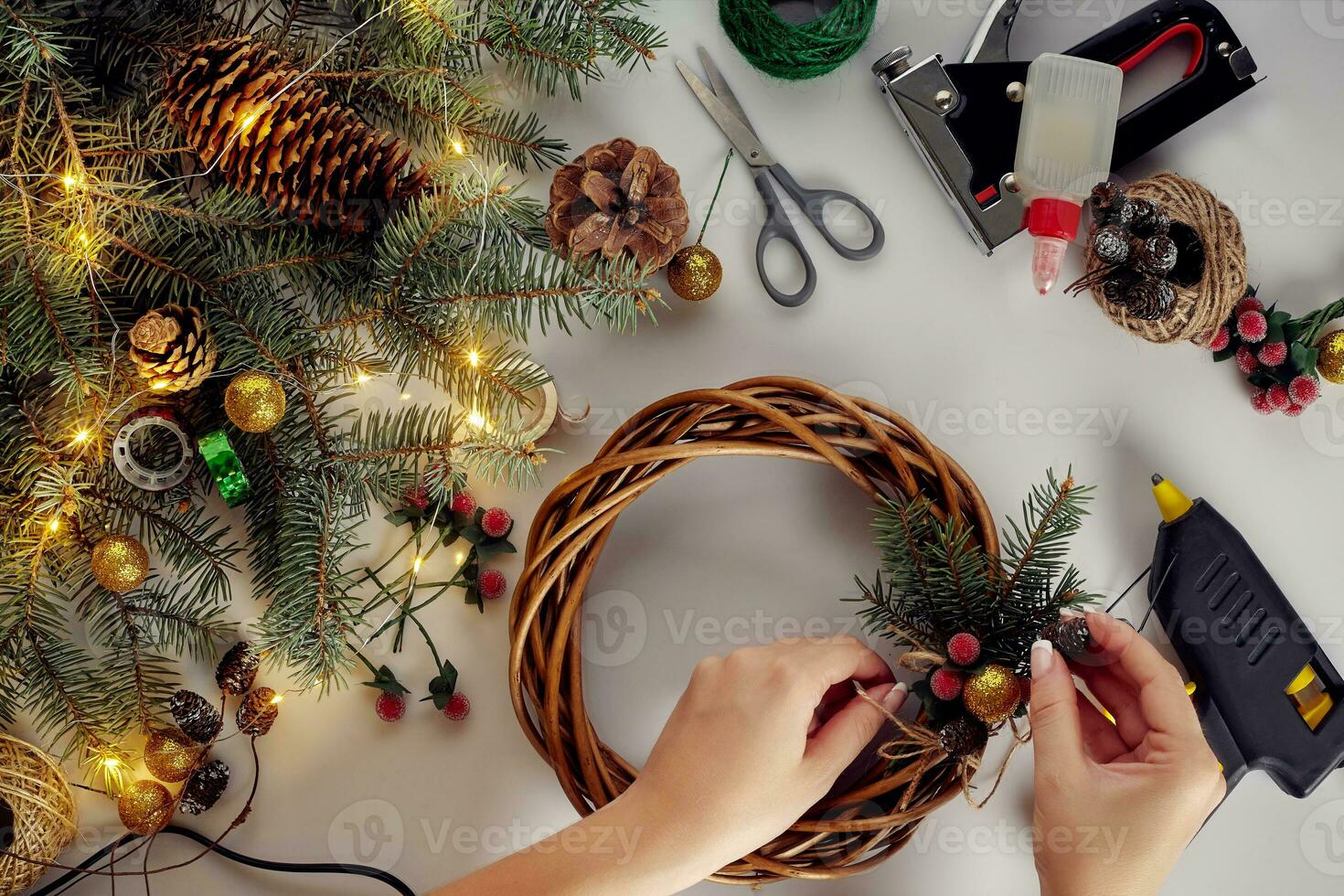 Top view of female hands make a Christmas wreath. Packed gifts and scrolls, spruce branches and tools on white table. photo