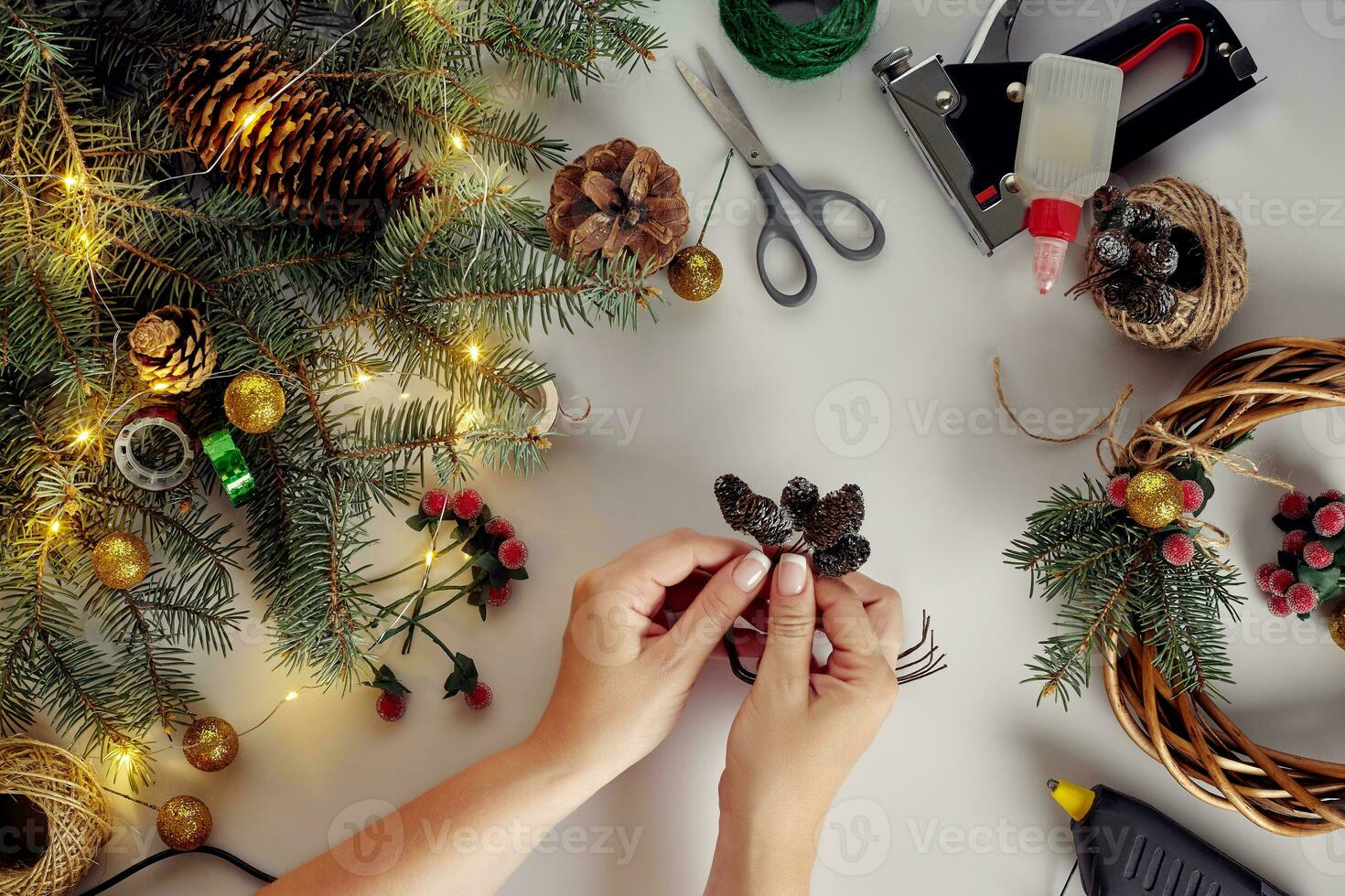 Female hands decorate the Christmas wreath with spruce branches with a red berry and forest cones. White background. New Year's concept. photo