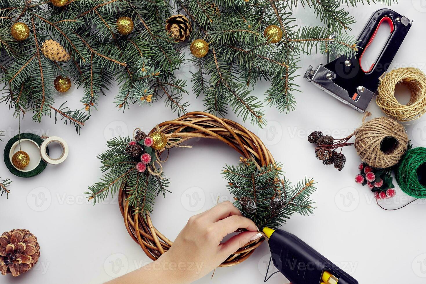 Top view of female hands make a Christmas wreath. Packed gifts and scrolls, spruce branches and tools on white table. photo