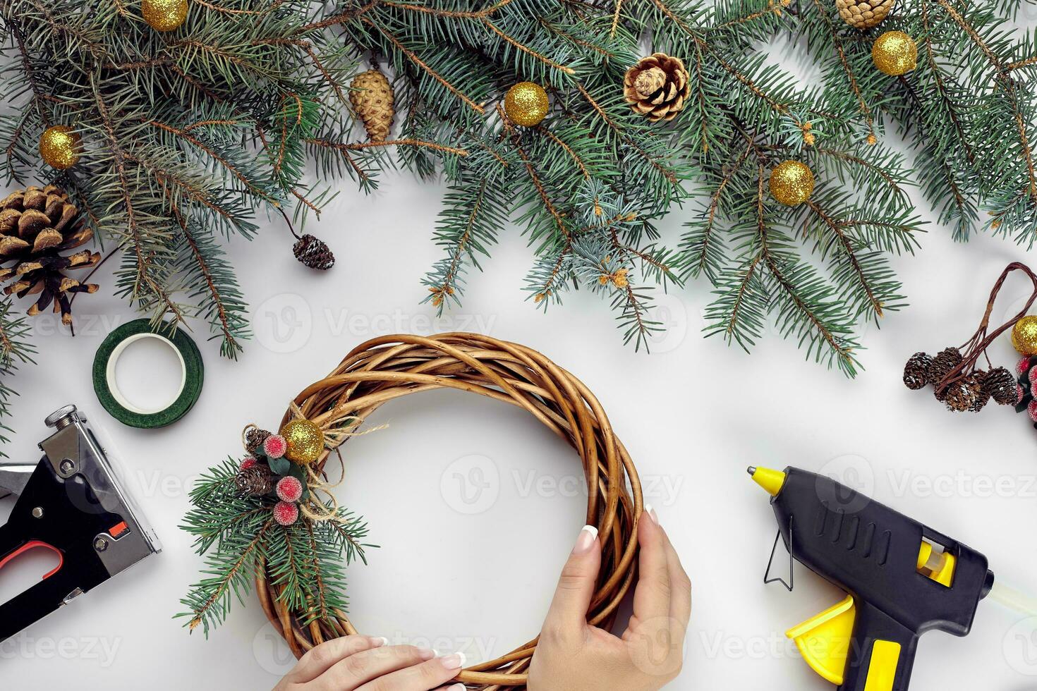 Top view of female hands make a Christmas wreath. Packed gifts and scrolls, spruce branches and tools on white table. photo