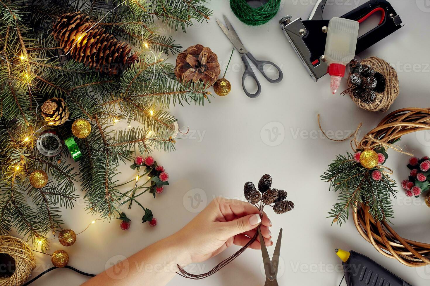Top view of female hands make a Christmas wreath. Packed gifts and scrolls, spruce branches and tools on white table. photo