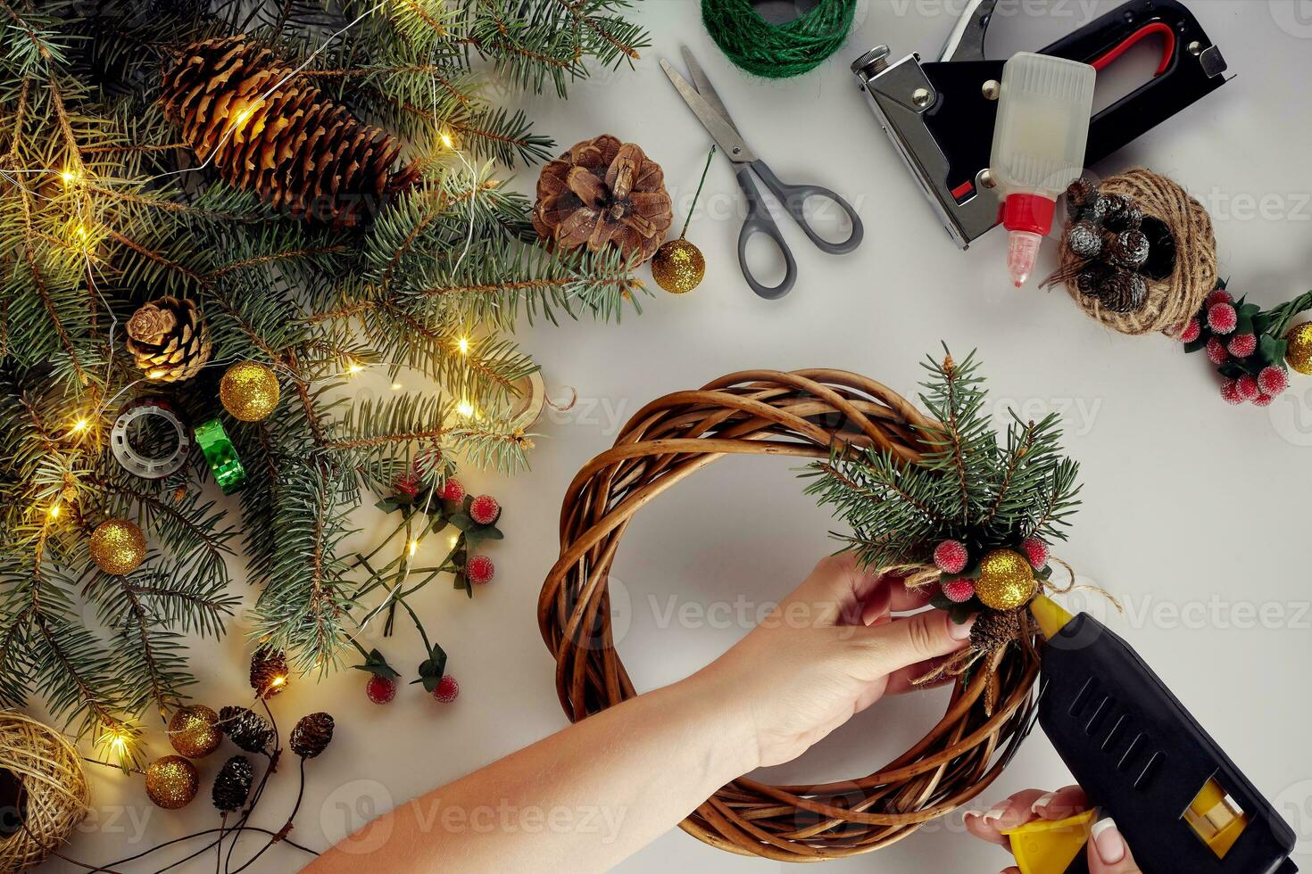 Top view of female hands make a Christmas wreath. Packed gifts and scrolls, spruce branches and tools on white table. photo
