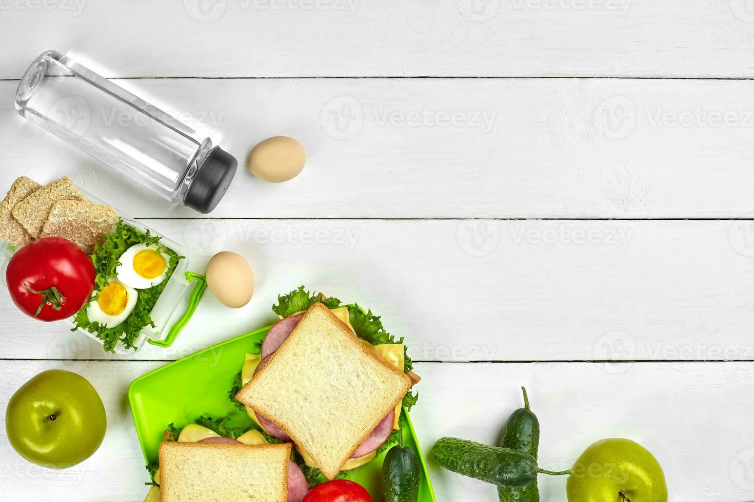 Healthy lunch box with sandwiches, eggs and fresh vegetables, bottle of water on rustic wooden background. Top view with copy space photo