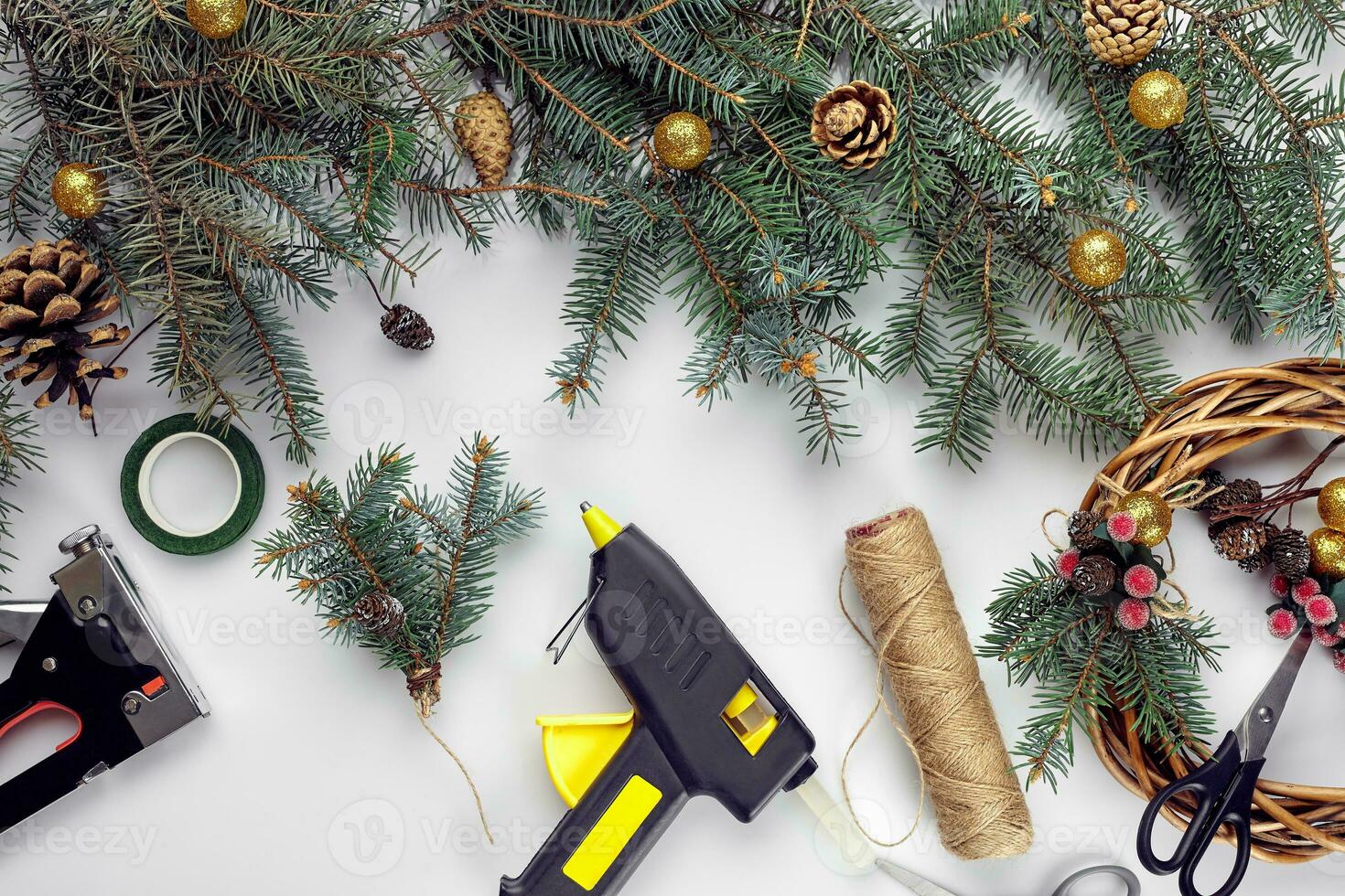 Top view of female hands make a Christmas wreath. Packed gifts and scrolls, spruce branches and tools on white table. photo