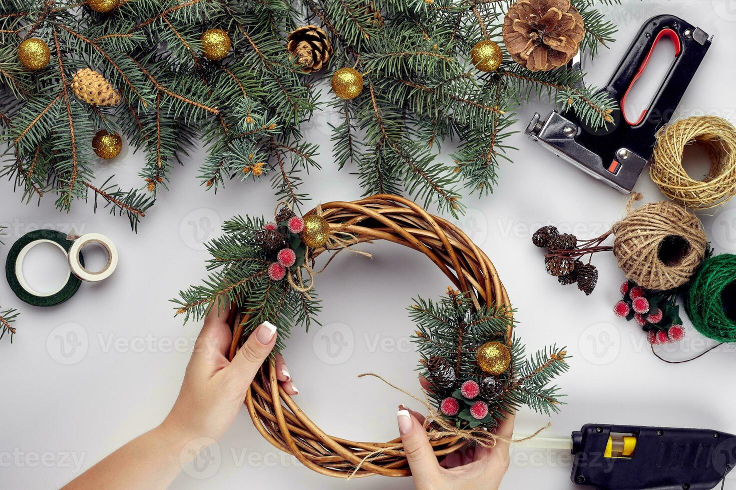 Top view of female hands make a Christmas wreath. Packed gifts and scrolls, spruce branches and tools on white table. photo