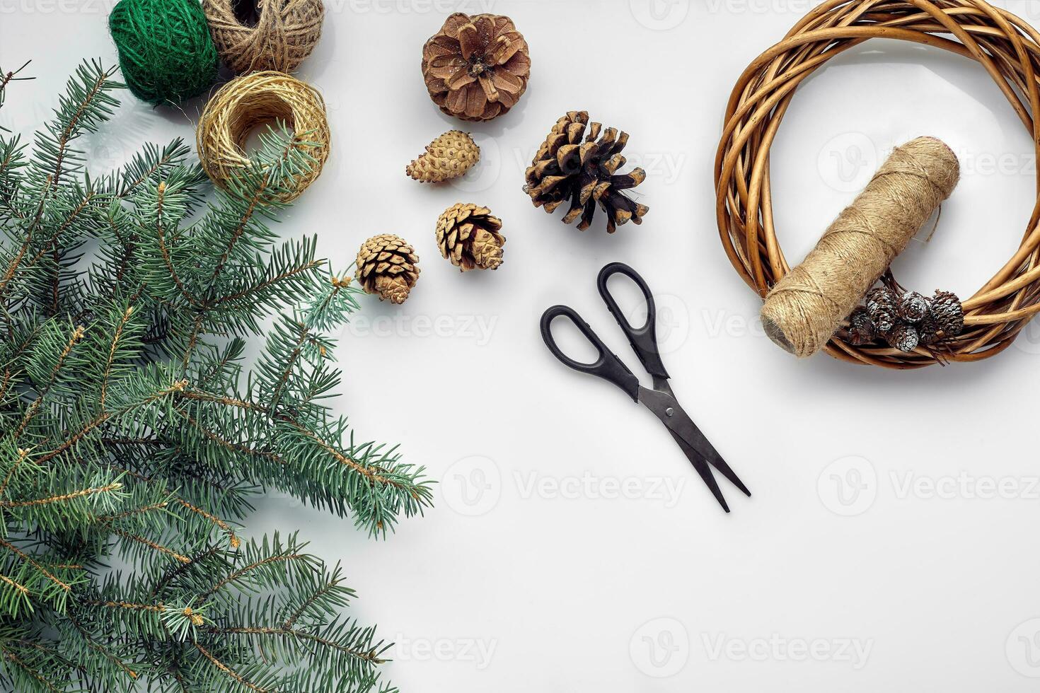 Beautiful festive handmade wreath base with three bumps near it, threads and twigs blue Christmas tree on the white table background, flat lay. photo