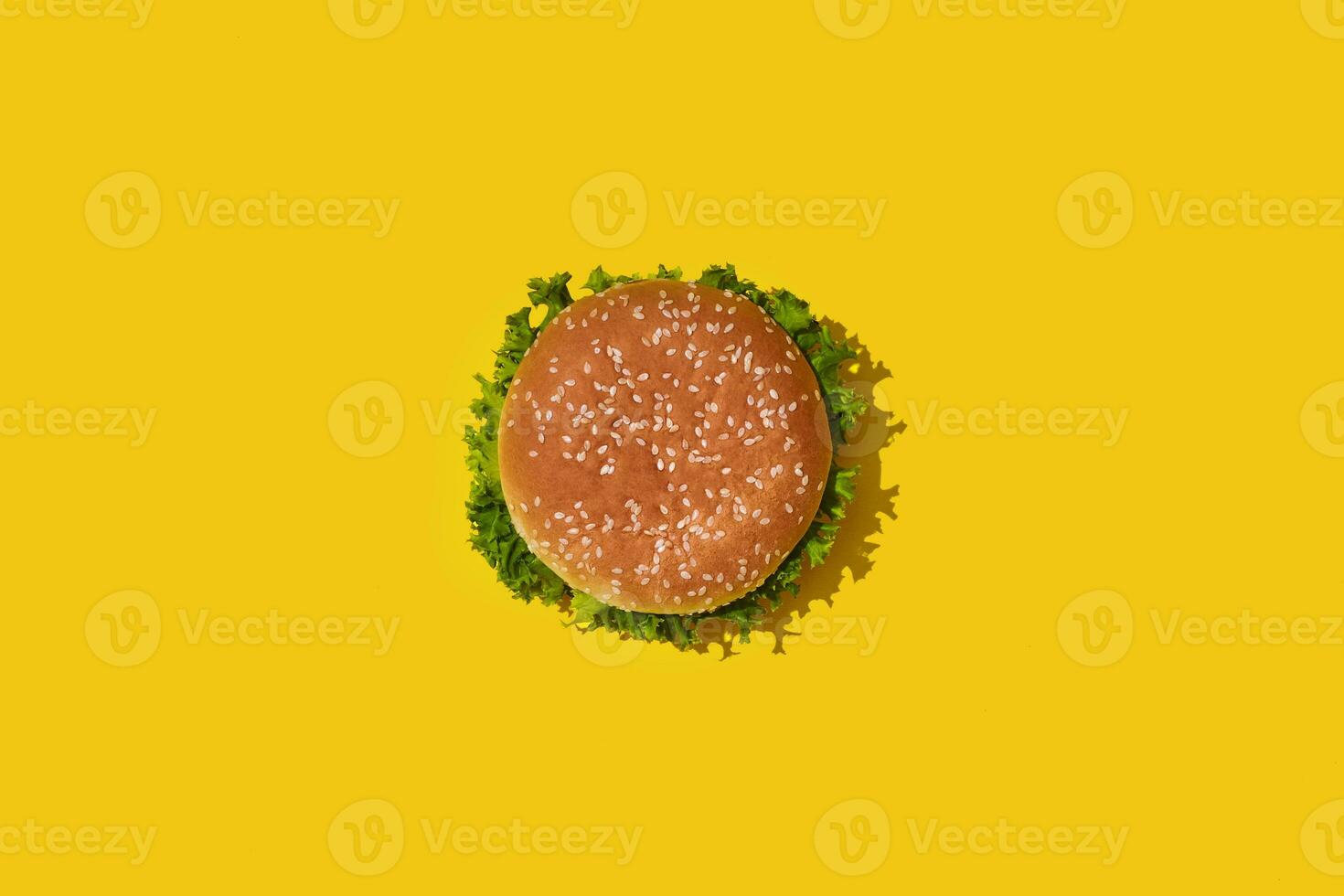 Tasty fresh unhealthy hamburger with ketchup and vegetables on yellow vibrant bright background. Top View with Copy Space. photo