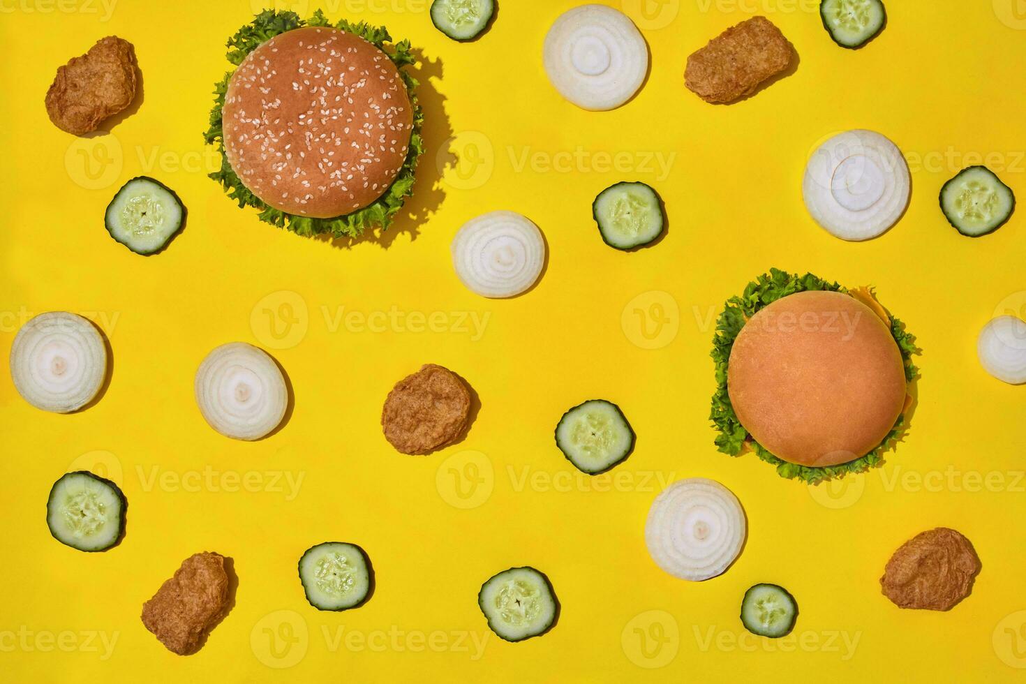 Most popular fast food meal. Chicken nuggets, burgers with fresh cucumber and onions on yellow background top view photo