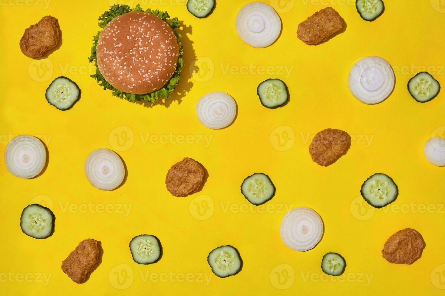 Most popular fast food meal. Chicken nuggets, burger with fresh cucumber and onions on yellow background top view photo