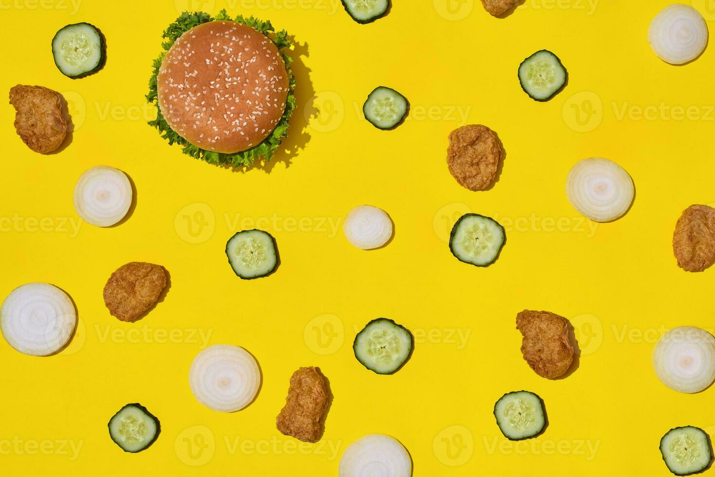Most popular fast food meal. Chicken nuggets, burger with fresh cucumber and onions on yellow background top view photo
