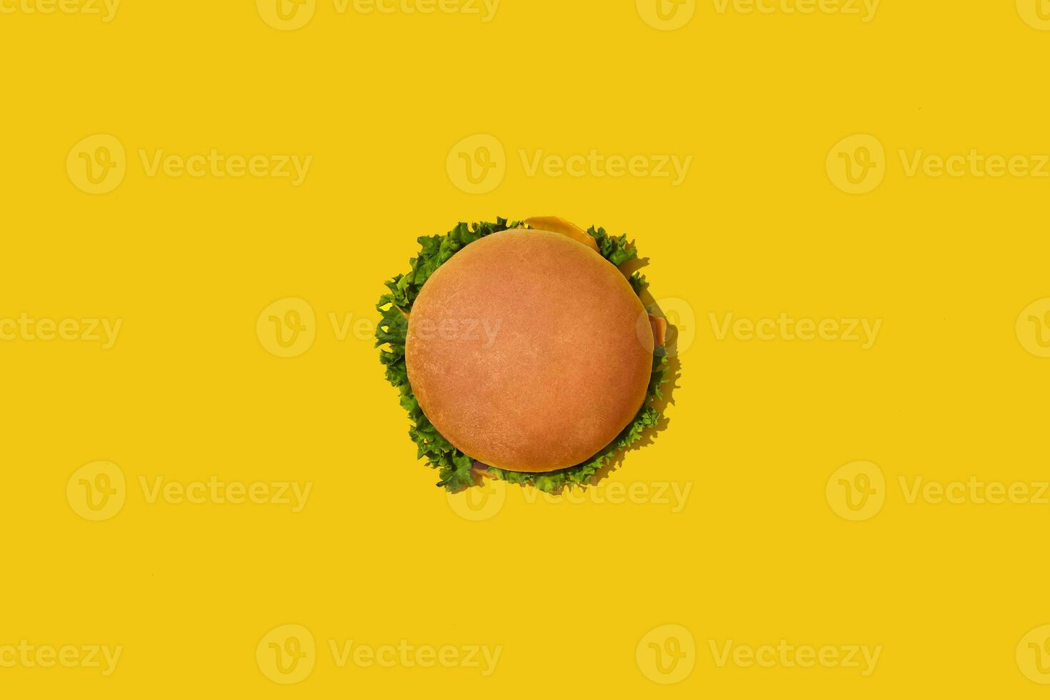 Tasty fresh unhealthy hamburger with ketchup and vegetables on yellow vibrant bright background. Top View with Copy Space. photo