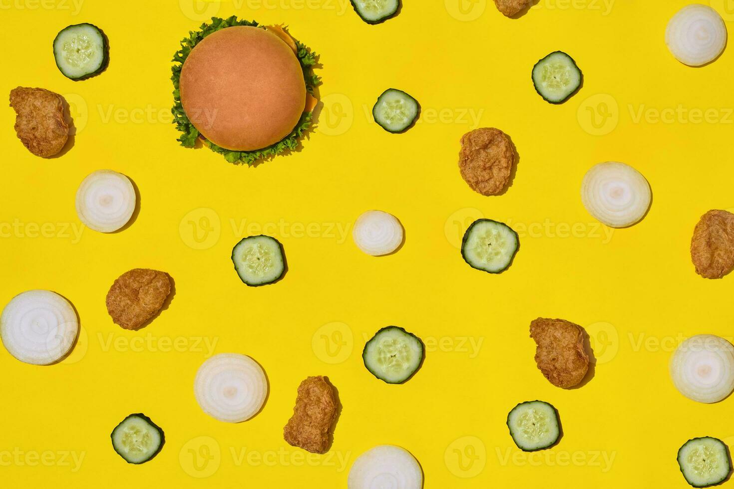 Most popular fast food meal. Chicken nuggets, burger with fresh cucumber and onions on yellow background top view photo