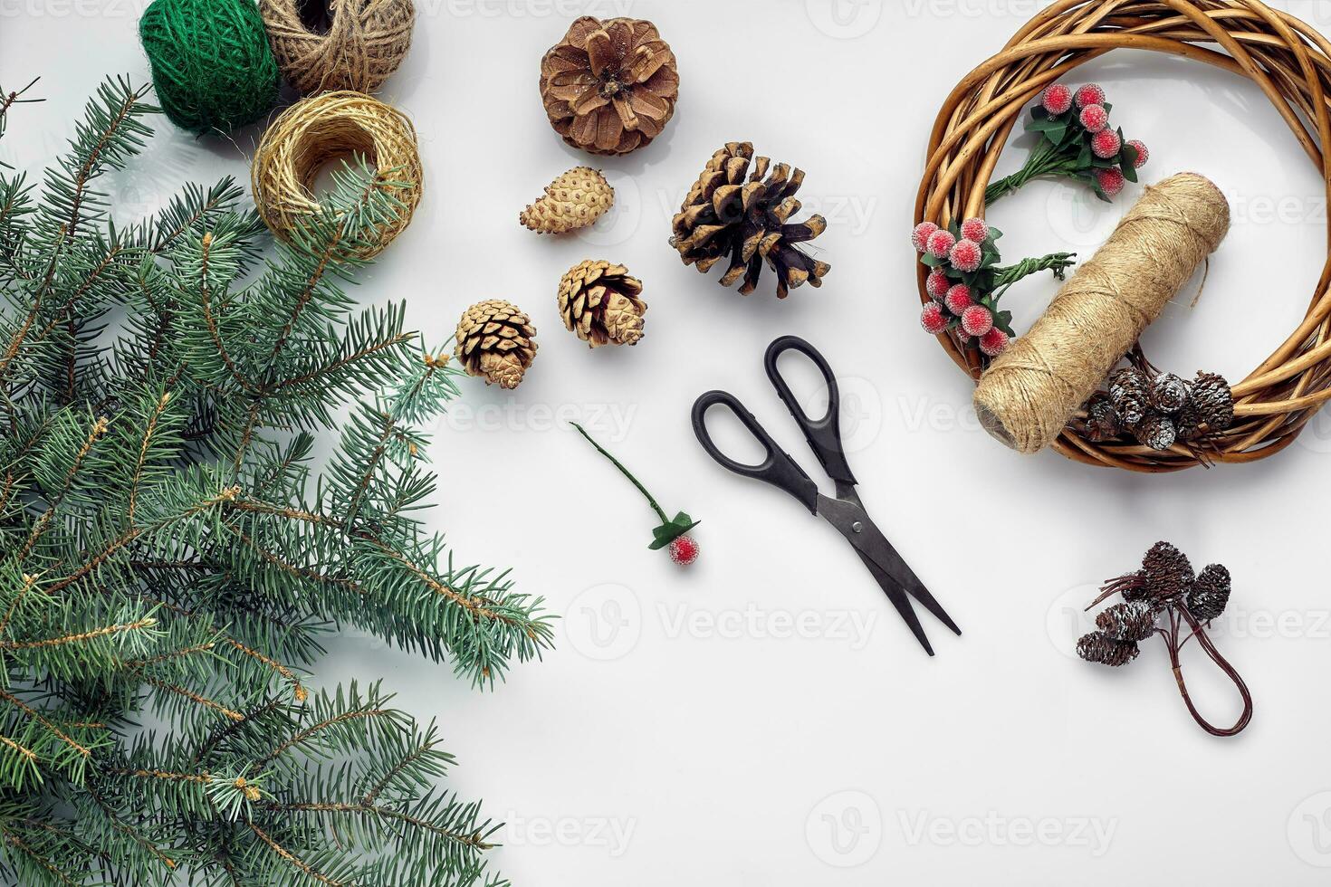 Beautiful festive handmade wreath base with three bumps near it, threads and twigs blue Christmas tree on the white table background, flat lay. photo