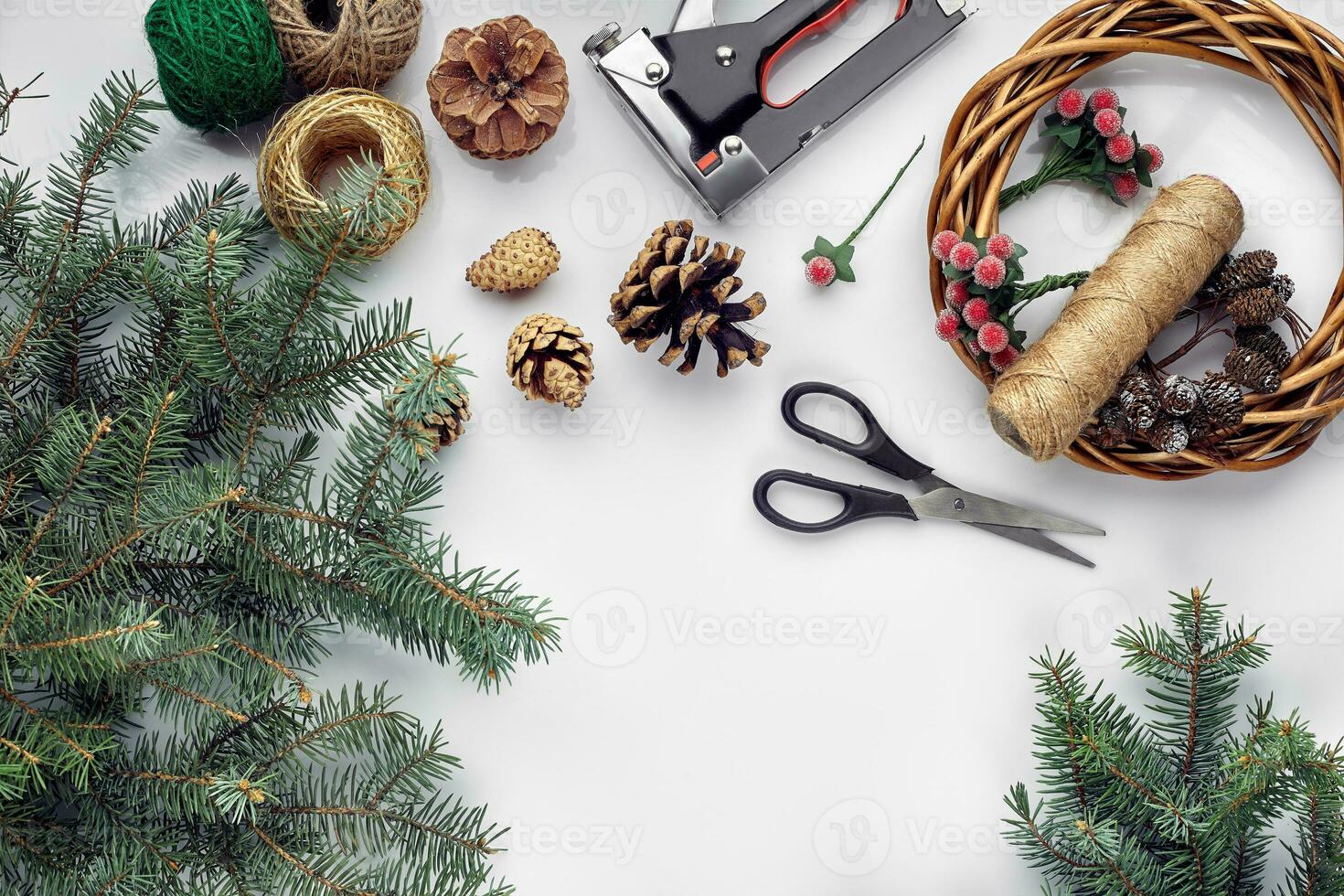 Beautiful festive handmade wreath base with three bumps near it, threads and twigs blue Christmas tree on the white table background, flat lay. photo