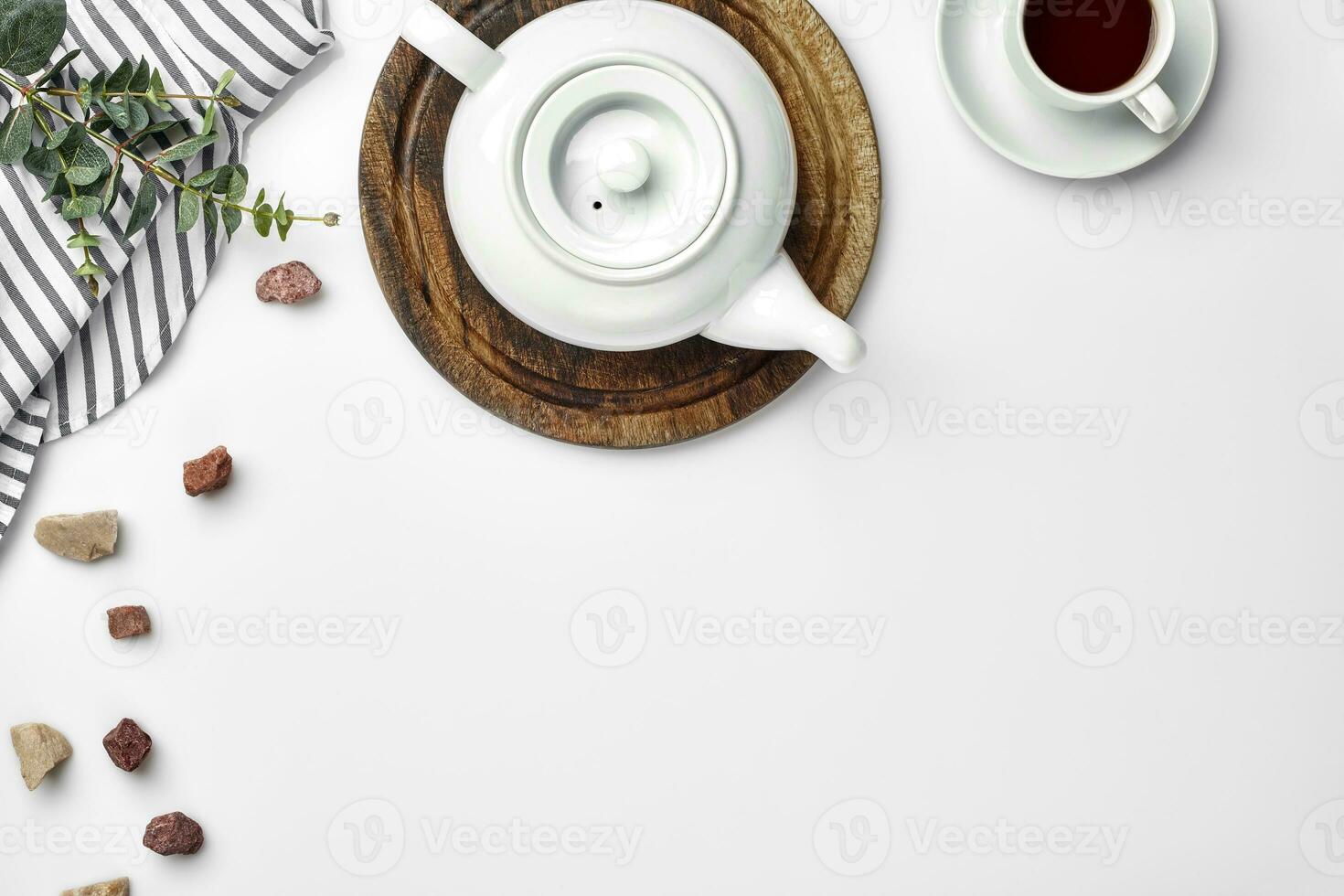 A white porcelain teapot on a wooden board and a white cup with tea on a table. Top view. Copy space. photo