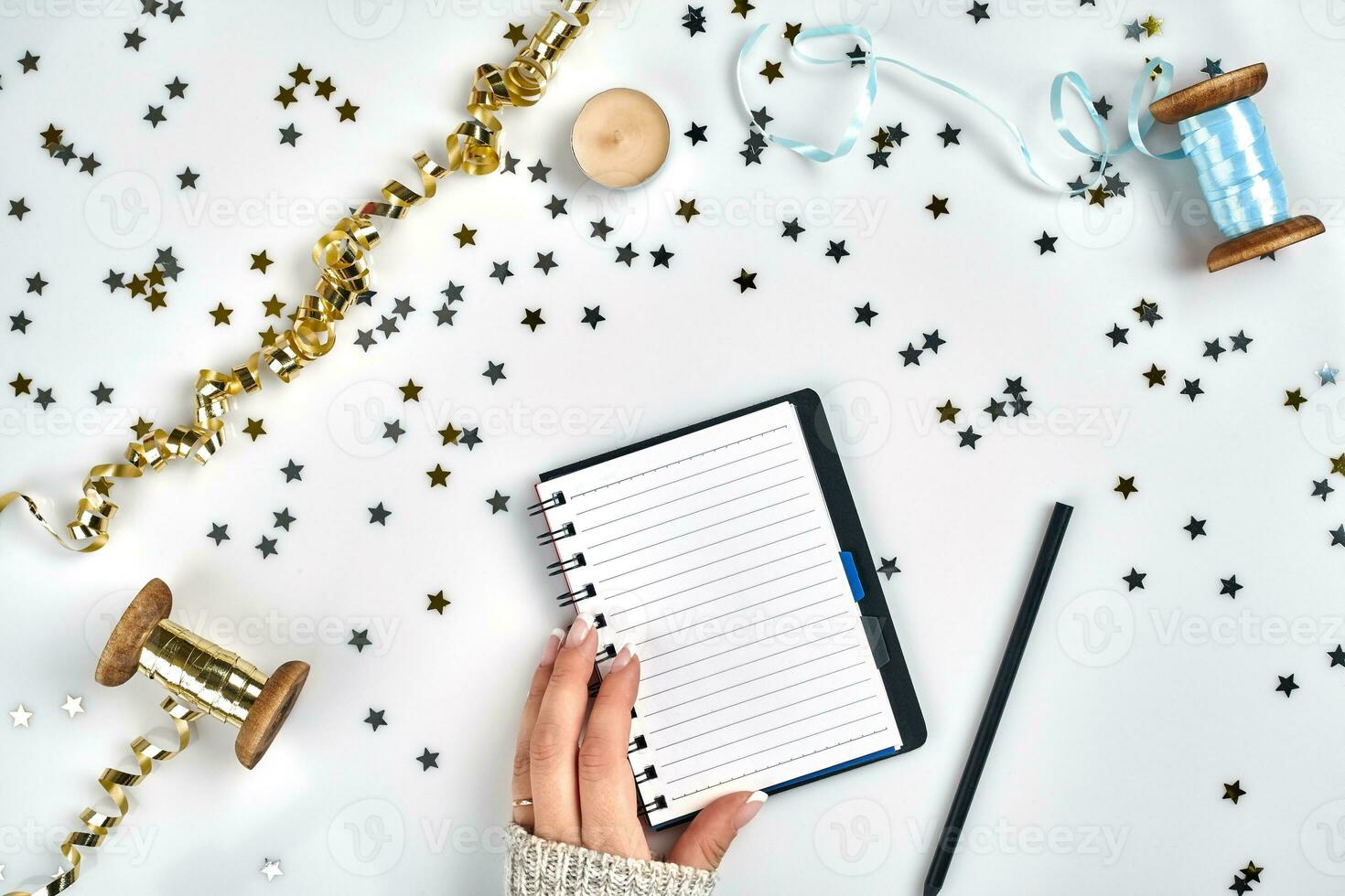 Festive decorations, delicate wavy ribbons, metallic star shaped confetti and notebook with wish list on white table, flat lay style. Christmas holidays decoration concept. photo
