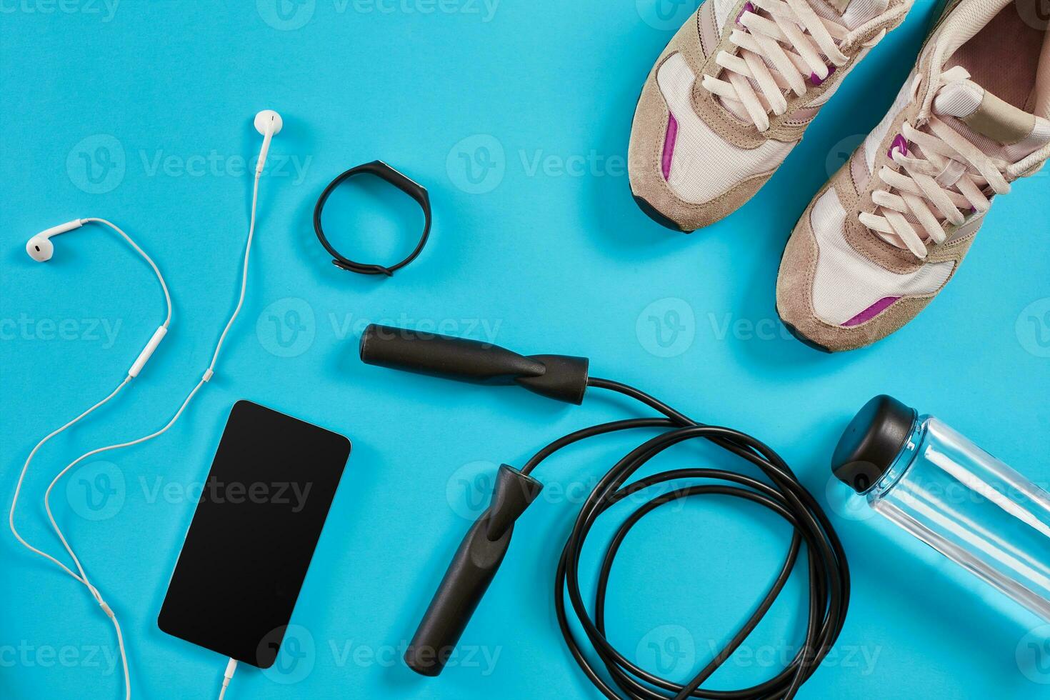 Flat lay shot of Sport equipment. Sneakers, jump rope, earphones and phone on blue background. photo