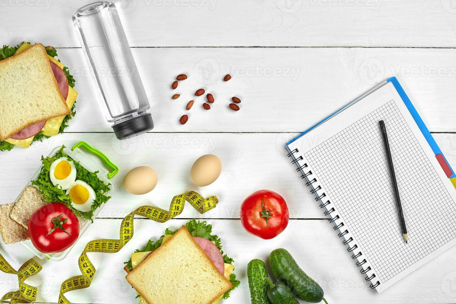 Top view planning notebook with copy space and healthy breakfast. Sandwich with ham and cheese, eggs, cucumber, tomato and bottle of water on white wooden table. photo