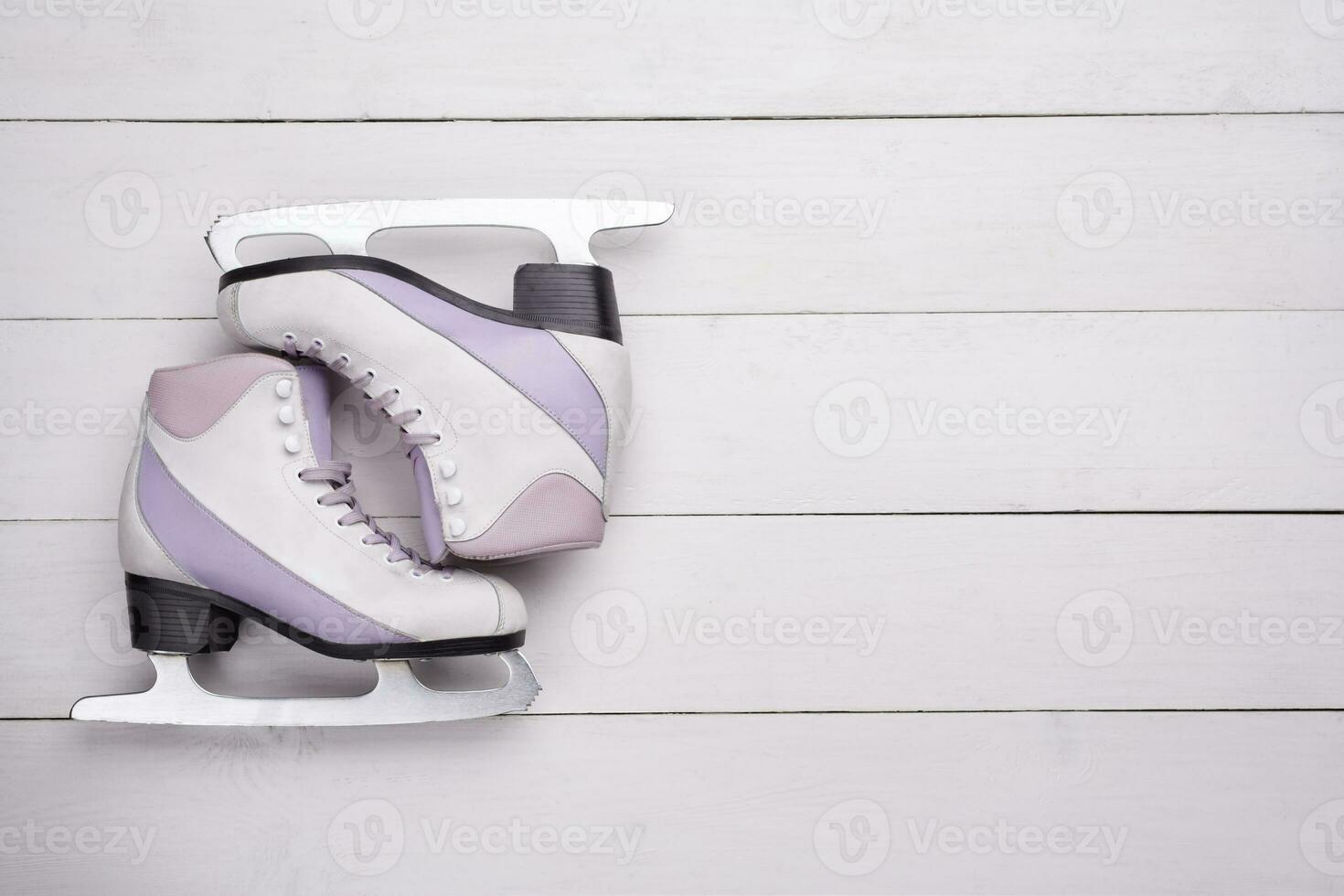 Close-up photo of professional ice skates lying on a white wooden background.