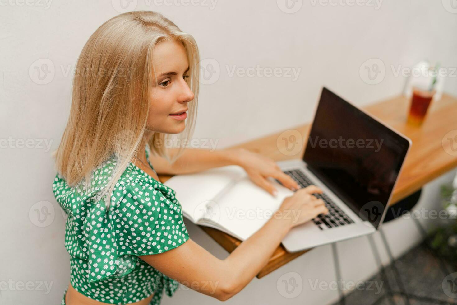 Pretty blond woman using lap top, making notes photo