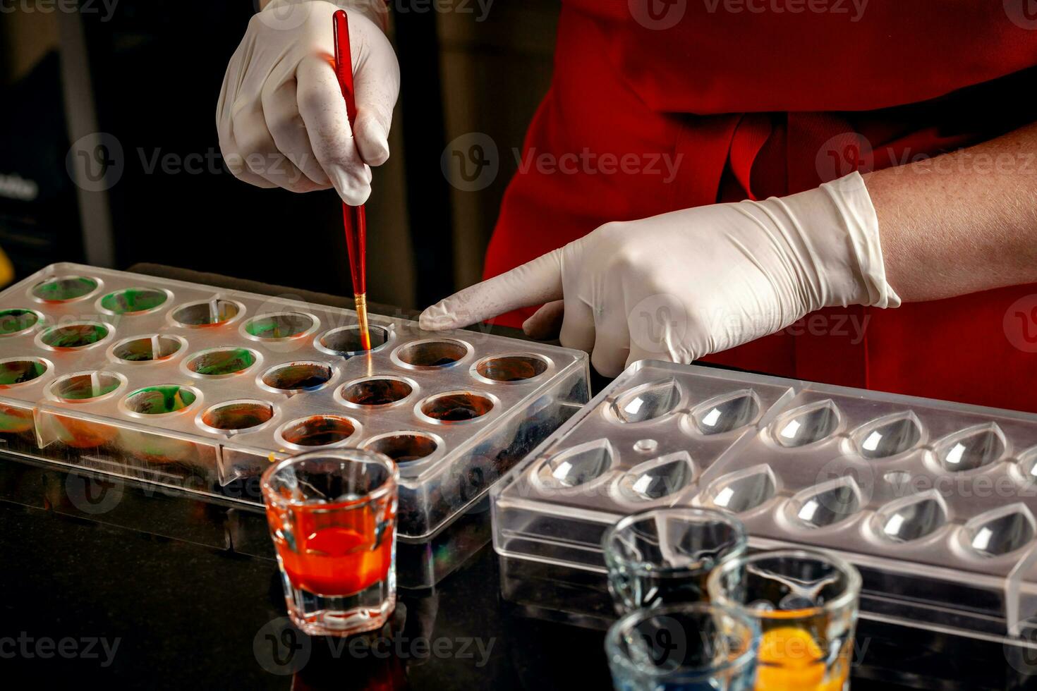 A woman confectioner with red uniform and white sterile gloves do a set of colorful chocolates from milk chocolate on a table. photo