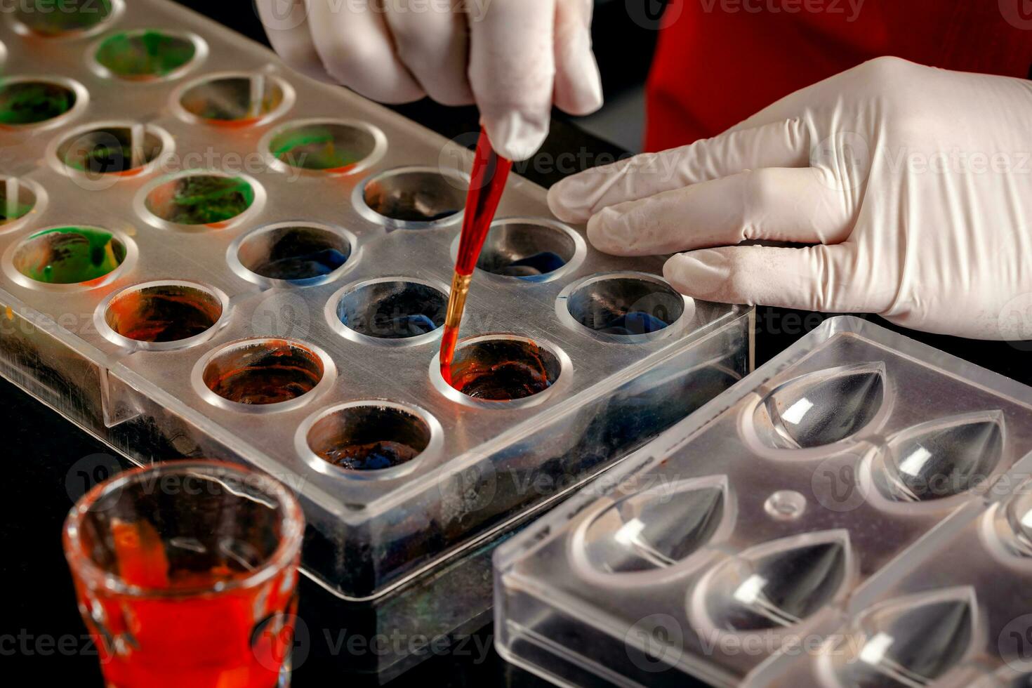 A woman confectioner with red uniform and white sterile gloves do a set of colorful chocolates from milk chocolate on a table. photo