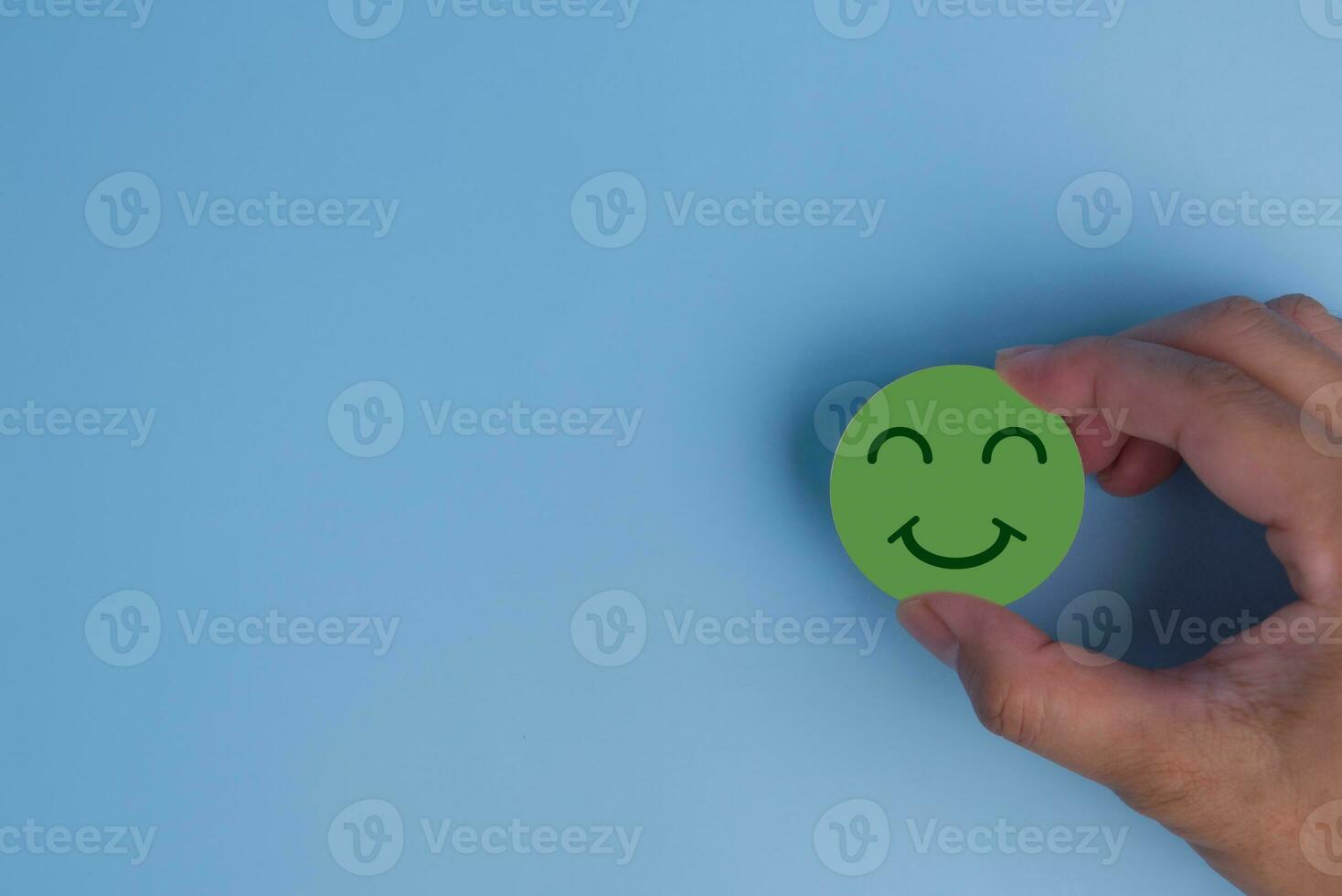 customer service evaluation and satisfaction survey concept. hand holding emotion happy smile face icon on wooden cube on blue background. copy space photo