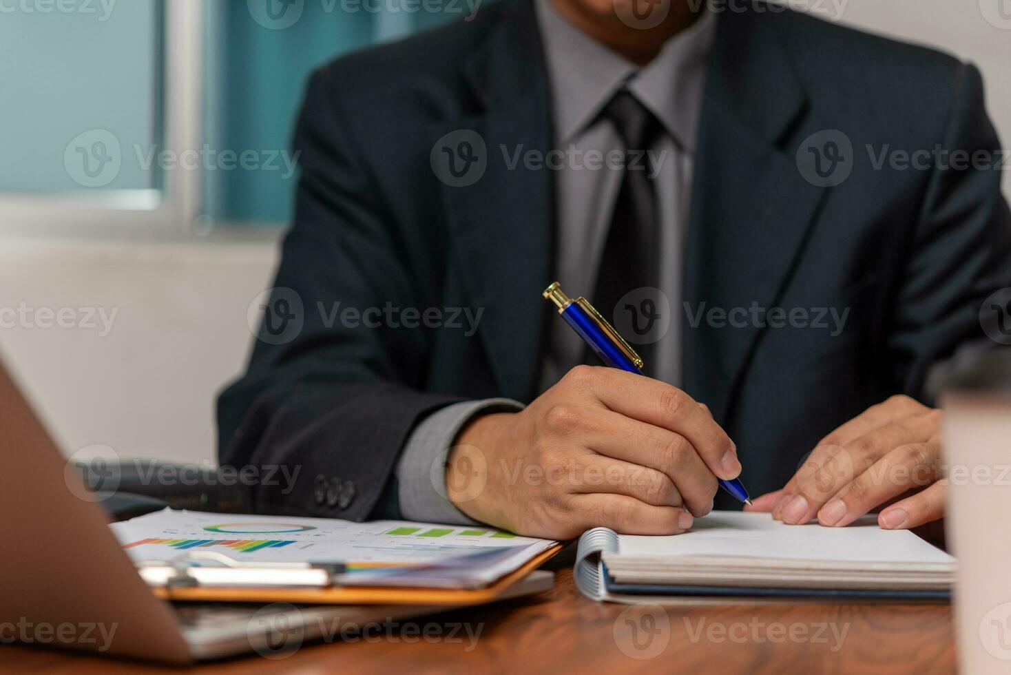 Businessman working at office with laptop and documents analyzing graphs and taking notes on desk. Business holding pen and paper notes chart marketing finance investment management photo
