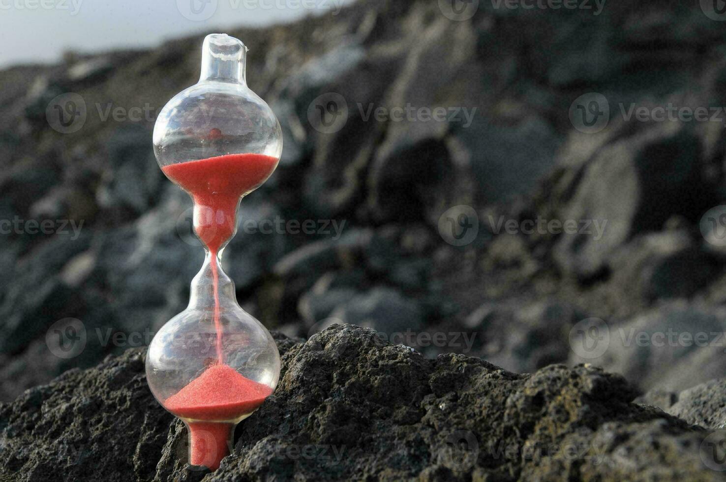 un rojo arena reloj de arena sentado en parte superior de un rock foto