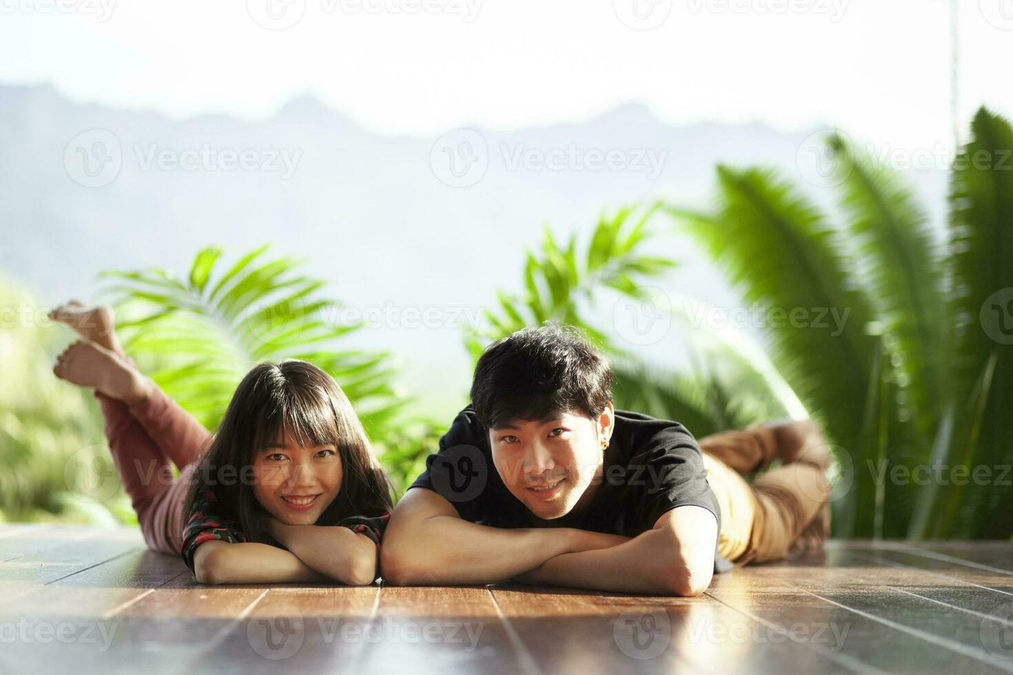 couples of younger asian man and woman lying with happiness face on home wood floor photo