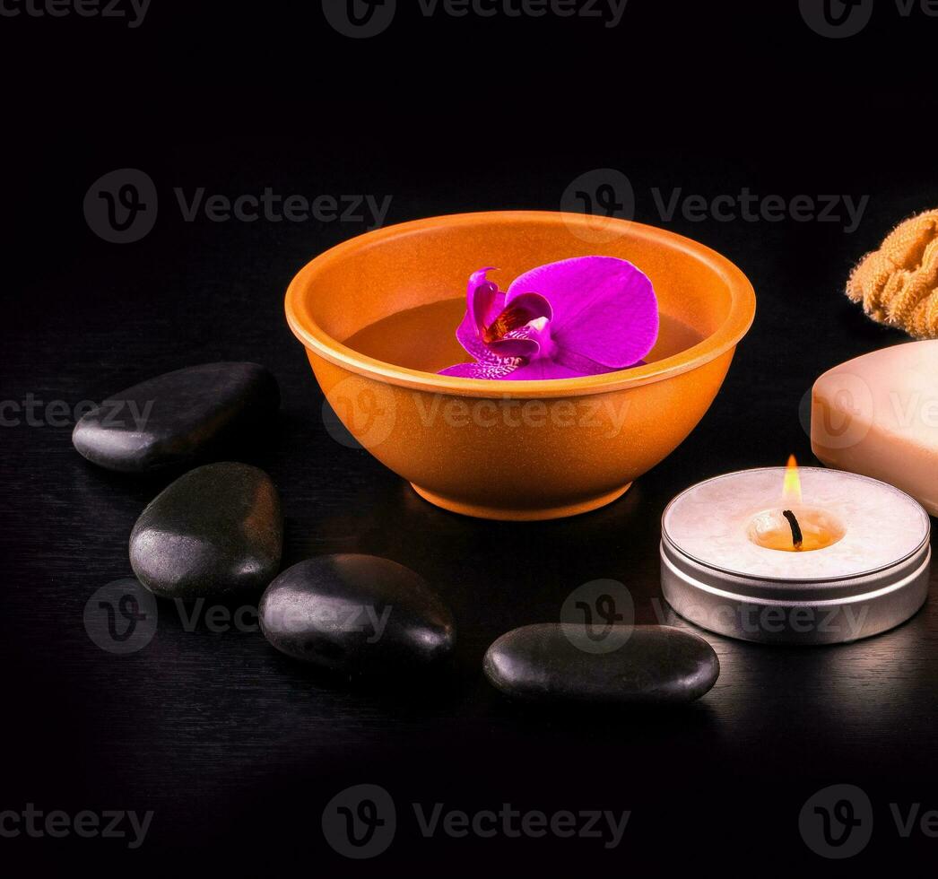 Beautiful spa composition with pink orchid on cup, stones and white gloves on black wooden table. photo