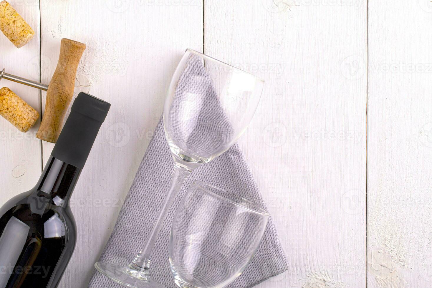 empty glasses, bottle of red wine and corkscrew on white wooden surface photo